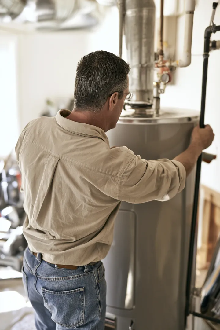 Man in his fifties installing a new water heater in a tidy home garage, seen over his shoulder