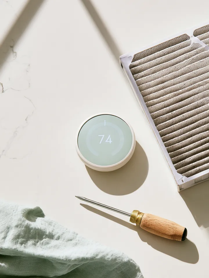 Smart thermostat, pleated air filter and small screwdriver set laid out on a white quartz counter