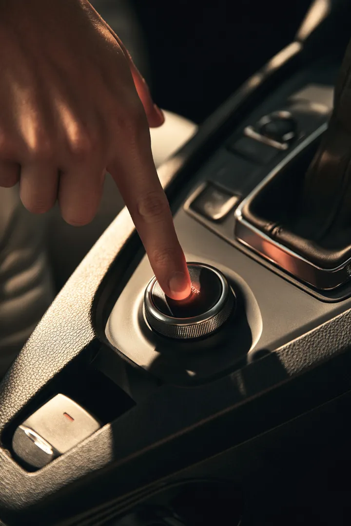 Finger pressing the push-start button on the dashboard of a recent-model car